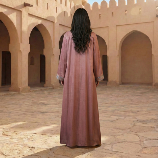 Woman in a long dress standing in front of a sandy-colored architectural structure.