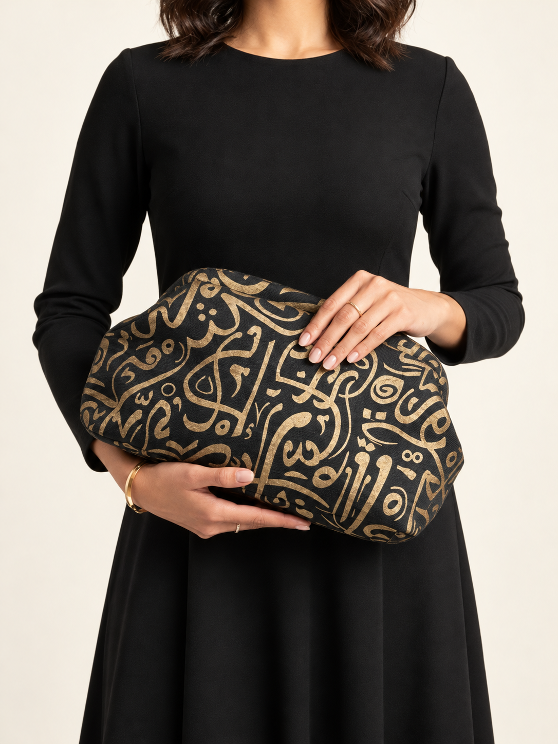 Black clutch with gold calligraphic pattern, carried by a model in a black dress