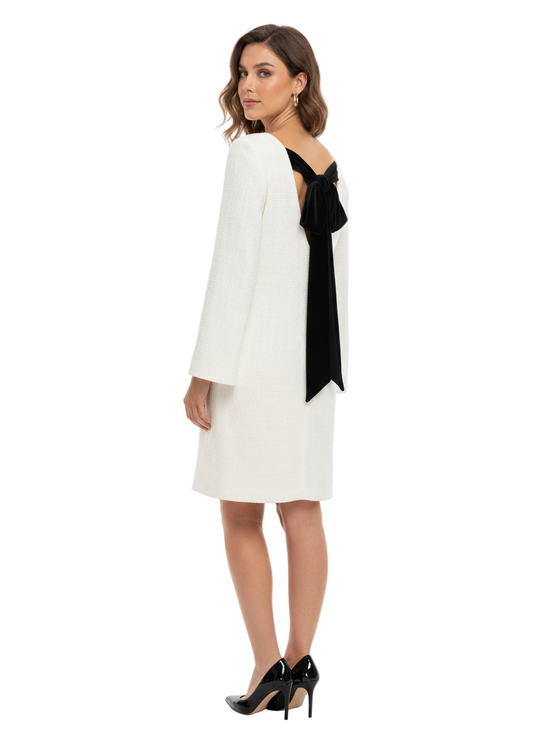 Woman wearing a white dress with a black bow detail on a white background